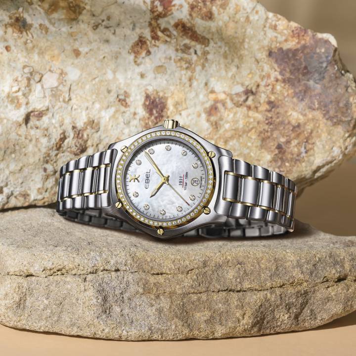 El Ebel 1911 Grande en oro amarillo de 18k y acero inoxidable tiene una esfera de nácar con índices de diamantes y un bisel engastado con diamantes.